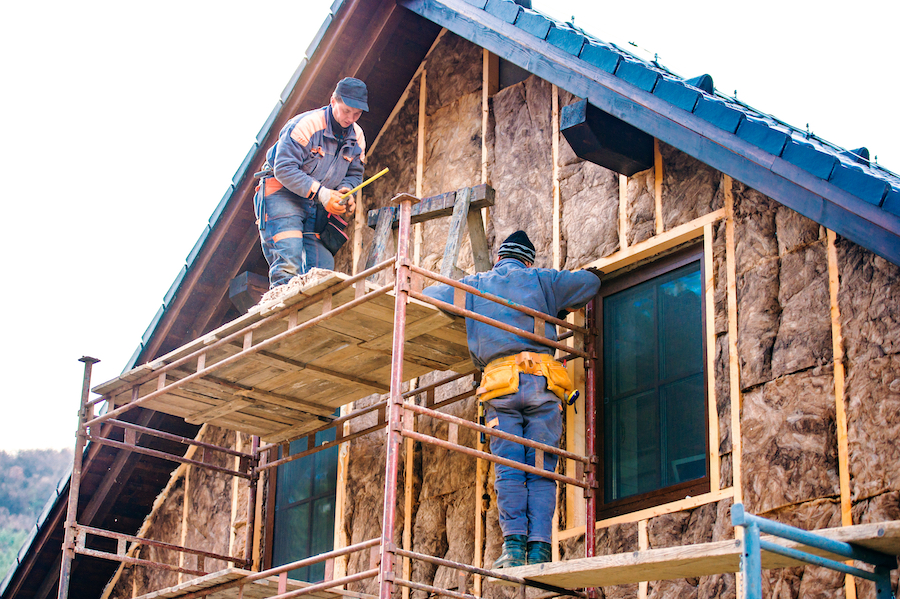 Construction workers standing on scaffold thermally insulating house facade with glass wool.